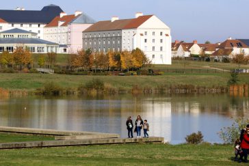 Au premier plan : lac et promeneurs. Au second plan : résidence touristique : hôtels B&B à Magny-le-Hongre