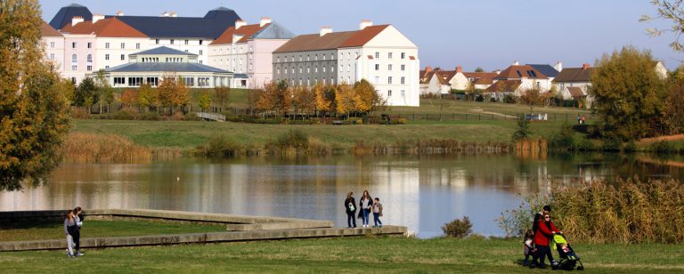 Au premier plan : lac et promeneurs. Au second plan : résidence touristique : hôtels B&B à Magny-le-Hongre